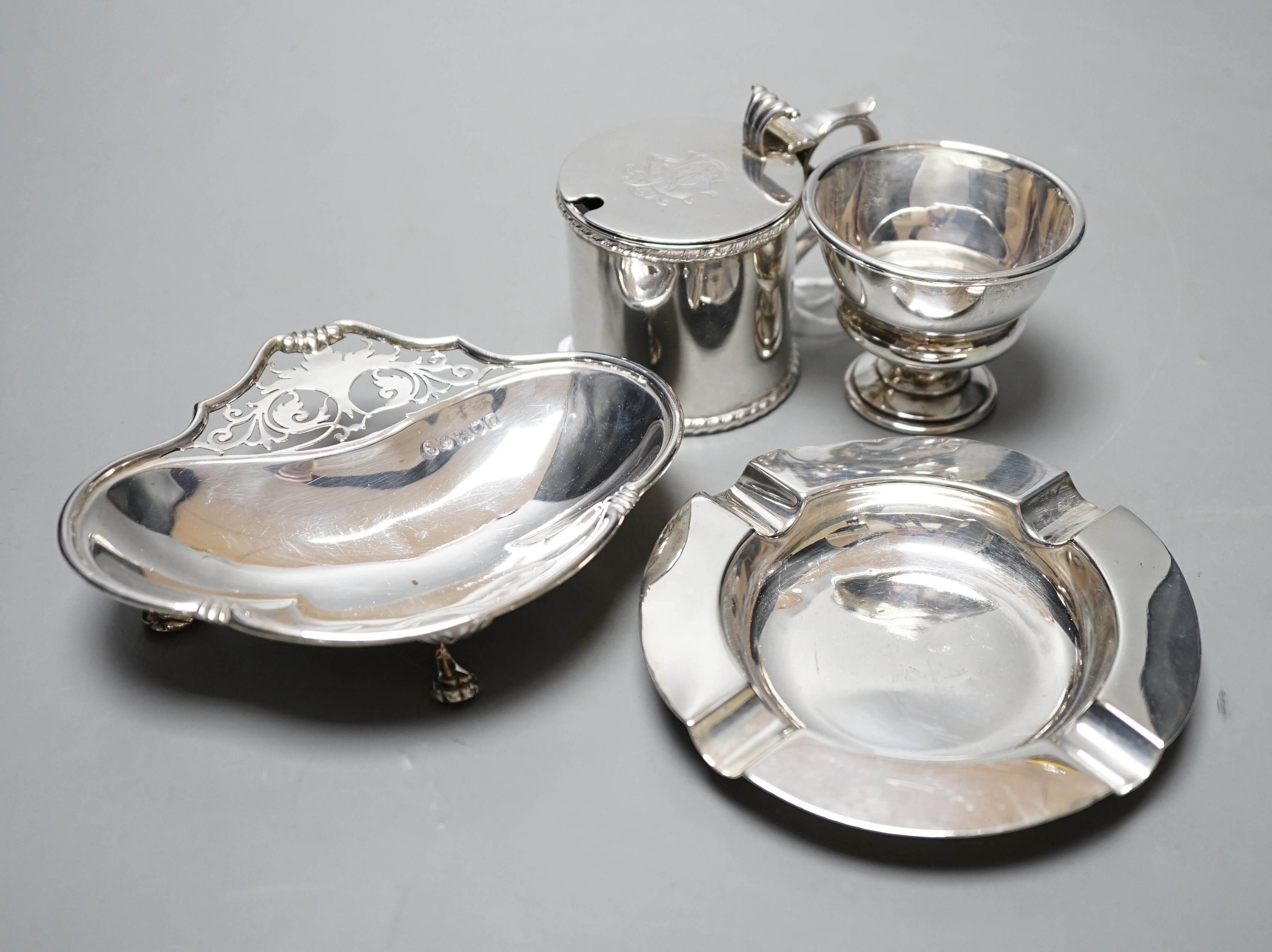A late Victorian silver mustard pot, Sheffield, 1896, a later silver ashtray and small bowl and an Edwardian pieced silver shaped dish by Elkington & Co, London, 1909.